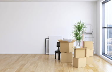 A spacious room with a large window, filled with stacked cardboard boxes ready for moving.