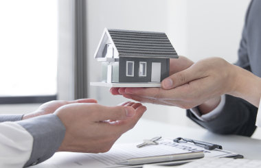 A miniature house resting on a hand, showcasing intricate details of the house's design, with a soft focus background emphasizing the hand's gesture.