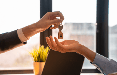 A hand passing a key to another hand, symbolizing the transfer of ownership or responsibility, with a soft focus background that highlights the action.