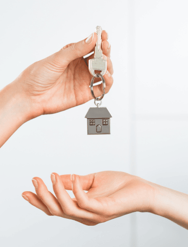A hand holding a house key, with a clear focus on the key’s details, against a blurred background that suggests a home setting.