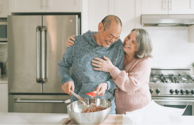 An elderly couple smiles joyfully at each other, displaying affection and happiness, with soft lighting that highlights their warm expressions.