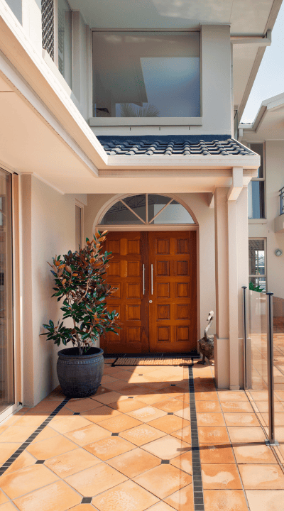 A modern house entrance with a pair of wooden double doors, a potted plant, and a tiled walkway.